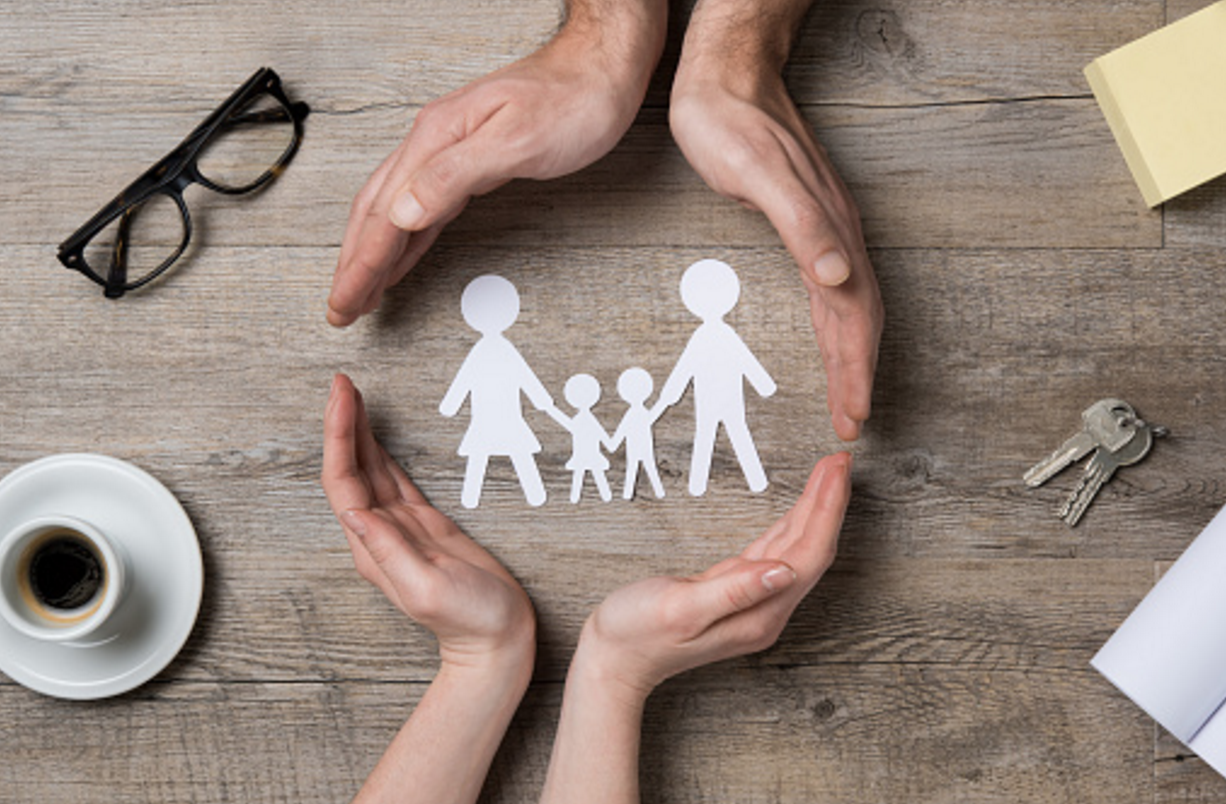 Hands surrounding a paper family cutout.