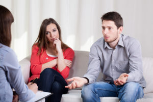 Man and woman sitting on couch having discussion with third party.